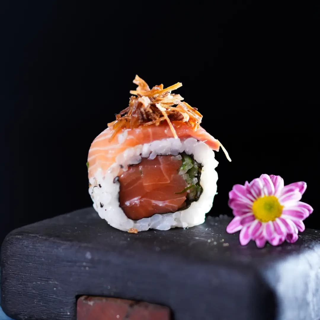 Uramaki Sharashi — Recheado com Salmão, Pepino Japonês, e por fora, Lâmina de Salmão, Calda de Maracujá Picante, Pimenta Sriracha e Alho Poró Crocante
